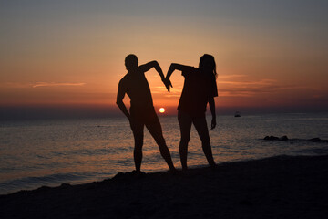 Romantic couple making heart on the beach with a beautiful sunset in background. Happy couple on summer vacation, love at sunset