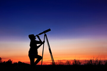 The child looks at the stars through a telescope. A teenager boy looks at the night sky through a spyglass against the backdrop of a sunset while in the field. - obrazy, fototapety, plakaty