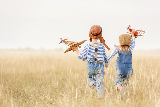 Boy and girl are running on the grass in the open air.
Cheerful and happy children play in the field and imagine themselves to be pilots on a sunny summer day. Kids dreams of flying and aviation.