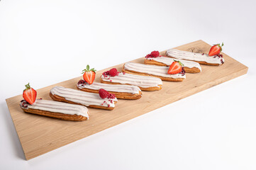 eclairs with glaze and strawberries on a wooden board, isolated on white, close up