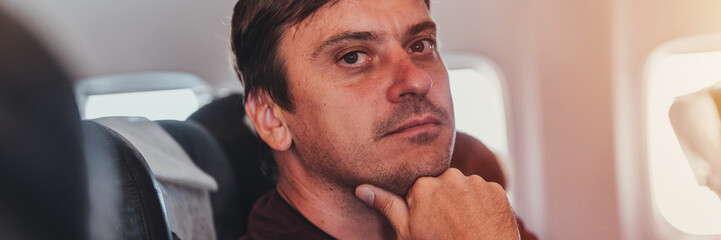 bored thoughtful unshaven people person man with 40+ years with stubble is sitting on a airplane during a flight from the airport to travel. spending time on the air plane. banner. flare