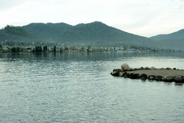 Obraz premium The ledge of the rocky shore overlooks the lake lying surrounded by high mountains overgrown with coniferous forest.