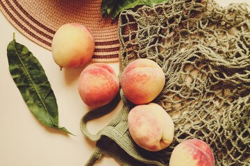 Many peaches, mesh bag and straw hat flat lay photography. Fresh summer fruits