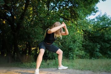 slender girl fitness model in a black tracksuit performs squats holding her hands in front of her