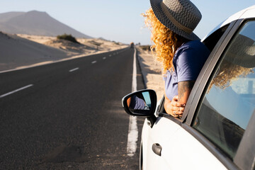 Woman enjoying road trip travel with car staying outside the window and admiring desert landscape outdoor. Traveler people for summer holiday vacation adventure lifestyle. Female driver and freedom