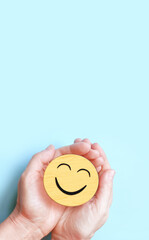 Hand holding happy smile face on blue background, Positive thinking, Mental health, World mental health day concept. - 521612676