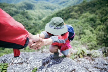 Person hike friends helping each other up a mountain. Man and woman giving a helping hand and...