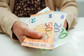 Retired elderly woman holding Euro banknotes money and worry about monthly expenses and treatment...