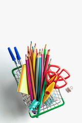 Shopping for school education supplies. Shopping basket with stationery on white background isolated, top view