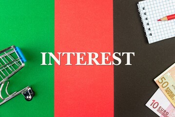 INTEREST - word (text) and euro money on a table of different colors, a trolley, a basket of grocery notepad and a red pencil. Business concept, buying, selling, supermarket, store (copy space).