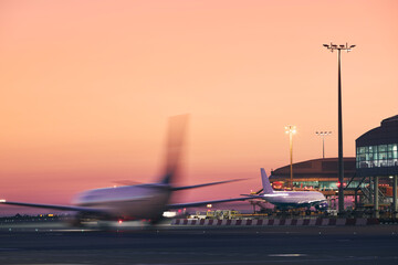 Airplane in blurred motion. Traffic at airport during colorful sunrise..