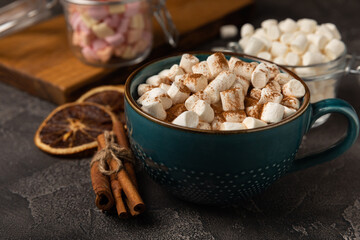 Cup of tasty cocoa drink and marshmallows in blue cup.Spices and marshmallows for winter drinks on black texture table.Winter hot drink.Hot chocolate with marshmallow and spices.Copy space.