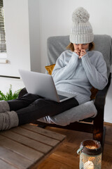 A woman in warm clothes with laptop. Low heating temperature in the house. Energy crisis concept	