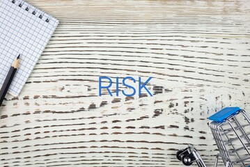 RISK - word (text), on a white wooden table, a notebook and a trolley, a grocery basket. Business concept: buying, selling, commerce (copy space).