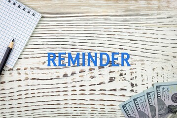 Naklejka premium REMINDER - word (text) and dollars on a white wooden table, notebook, notepad. Business concept: buying, selling, commerce (copy space).