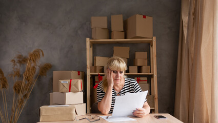Worried elderly female enterpreneur thinking on postal letter informing about debt. Anxious self...