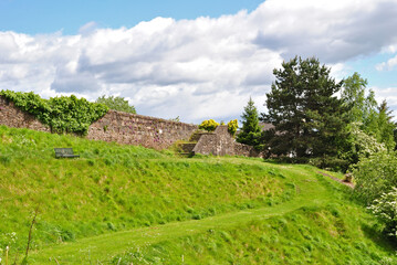 Obraz premium Steep Grassy Hillside with Paths and Stone Wall against Blue Cloudy Sky 