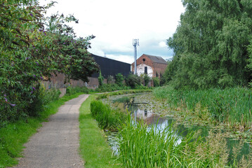 Obraz premium View Along Overgrown Canal and Towpath with Industrial Buildings 