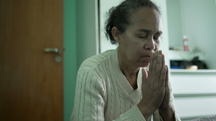 Brazilian older woman praying to God. Faithful and Spiritual elder lady prays by the bed