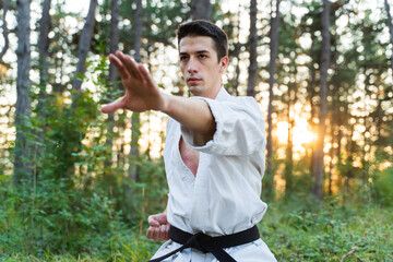 A young guy doing karate training and meditation in the forest during the day