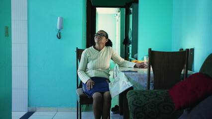 A pensive senior hispanic woman sitting at home alone. A thoughtful black mature older person