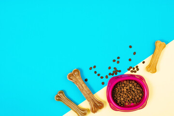 Dry dog pet food in bowl and accessories on blue background top view. Pet feeding and care concept background with copy space. Photograph taken from above.