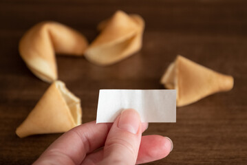 Person holds in hand blank paper slip from fortune cookie against few cookies laying on table...