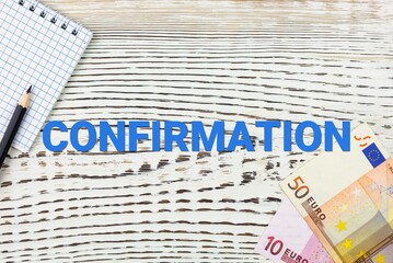 CONFIRMATION - word (text) and euro money on a white wooden table, notebook, notepad. Business concept: buying, selling, commerce (copy space).