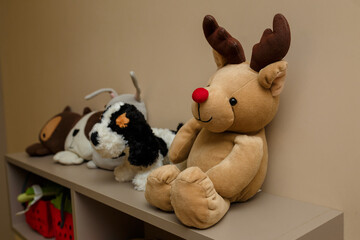 Cuddly toys of pet dogs and reindeer on shelf. Soft fabric stuffed animals in child room interior