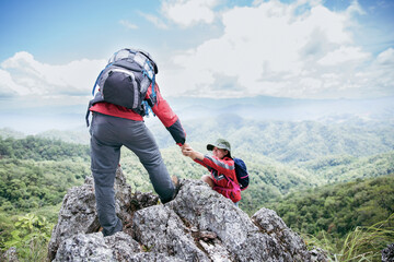 Person hike friends helping each other up a mountain. Man and woman giving a helping hand and...