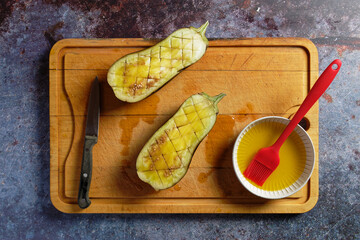 Halved eggplant is prepared for roasting. On a wooden cutting board.