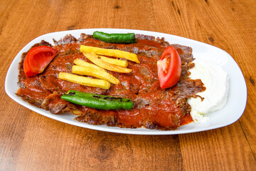 Turkish and Arabic Traditional Ramadan doner kebab with tasty tomato sauce and rice or turkish pilav in white plate on wood table background. ( , Iskender, ekmek arasi pilav ustu doner, doner durum )