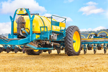 A fragment of a modern agricultural seeder against a yellow field and a blue sky.
