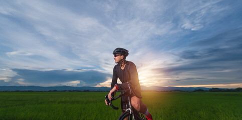 Fototapeta na wymiar Portrait of a handsome young man wearing a helmet cycling on the road with copy space. cornfield background on sunset