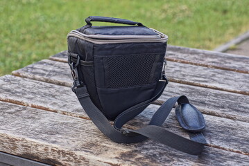 one black bag made of fabric with a harness stands on a gray wooden table on the street against the background of green grass