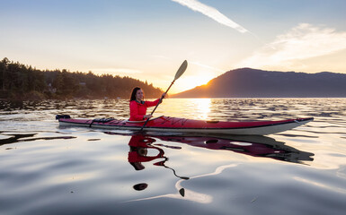 Adventurous Woman on Sea Kayak paddling in the Pacific Ocean. Sunny Summer Sunset. Taken near...