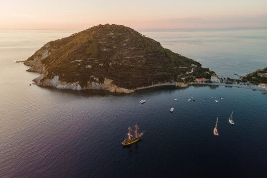 Aerial view of a pirate vessel sailing along the coast at sunset in Capo D'Enfola, Elba Island, Tuscany, Italy.