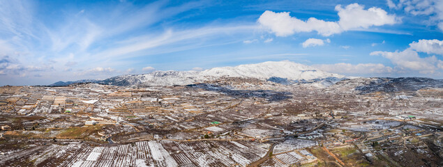 Aerial view of a valley with agricultural field in wintertime with snow and mountain in background, Golan Heights, Israel.