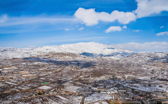 Aerial view of a valley with agricultural field in wintertime with snow and mountain in background, Golan Heights, Israel.