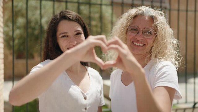 Two women mother and daughter hugging doing heart gesture with hands at street
