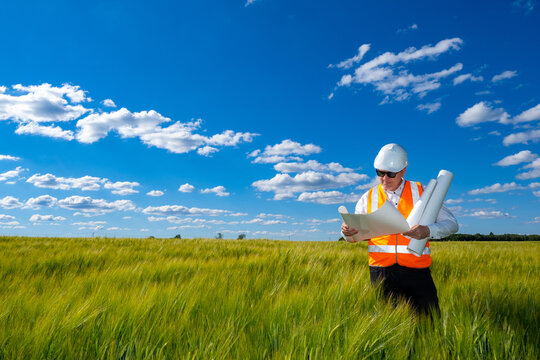 Man architect. Architect with papers on summer field. Man in construction worker uniform. Architect reviews construction drawings. Concept - choice of territory for construction of residential area