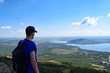 Naklejka premium A man with a backpack stands on a mountain and looks at the lakes on a summer day