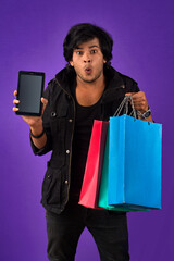 Portrait of a young man with a mobile phone or tablet smartphone and shopping bags in his hands.