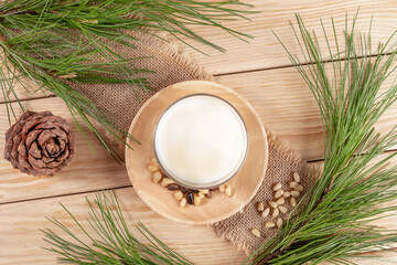 Vegan drink cedar milk in glass, nuts, branches on burlap napkin on wooden table. Top view.