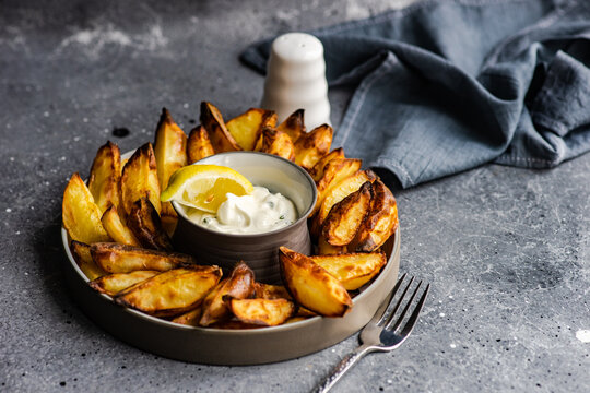 Close-up of a plate of baked potato wedges with sour cream, garlic and dill dip