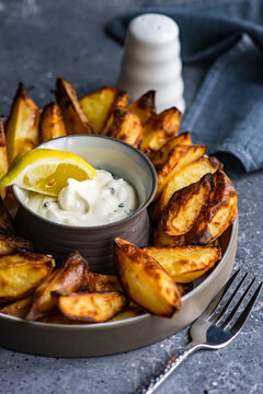 Close-up of a plate of baked potato wedges with sour cream, garlic and dill dip