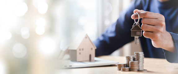 Businessman choosing mini wood house model from model and row of coin money on wood table,...