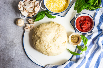 Overhead view of dough, tomato sauce, mushrooms, cheese, basil and oregano ingredients on a table for cooking an Italian pizza