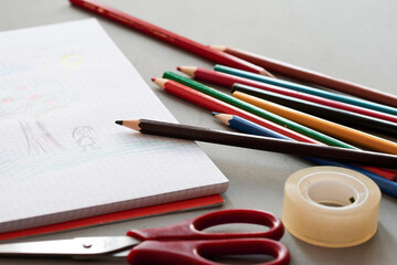 View of colored pencils next to a notebook with a drawing. Back to school concept.