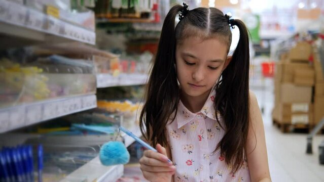 A preteen girl in a supermarket chooses a pen and paints it on a piece of paper.